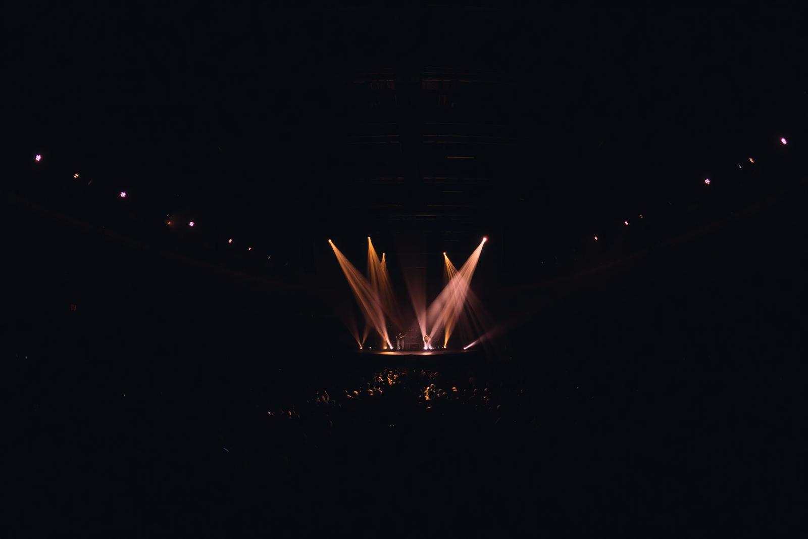 Salle de concert sombre traversée par des faisceaux lumineux